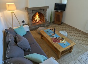Un salon avec une cheminée en pierre, un canapé, une table basse avec des collations et un téléviseur.