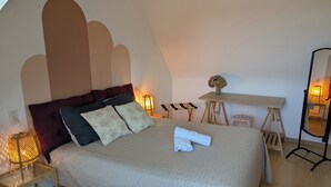 A neatly made bed with pillows, a bedside lamp, a small table with a vase, and a mirror. - Au coin du châtaignier (Saint-Georges-de-Reintembault)