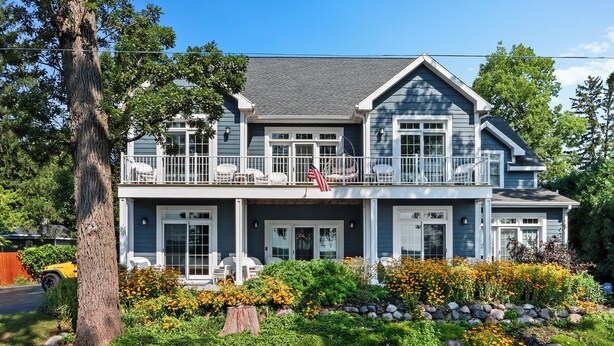A two-story house with a balcony, a front porch, and a well-maintained garden with various plants and flowers. - THE ULTIMATE LAKEHOUSE (Lake Geneva)