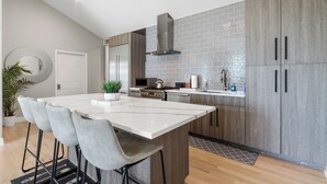 A modern kitchen with a large island, bar stools, a microwave, stove, and a sink. - THE ULTIMATE LAKEHOUSE (Lake Geneva)