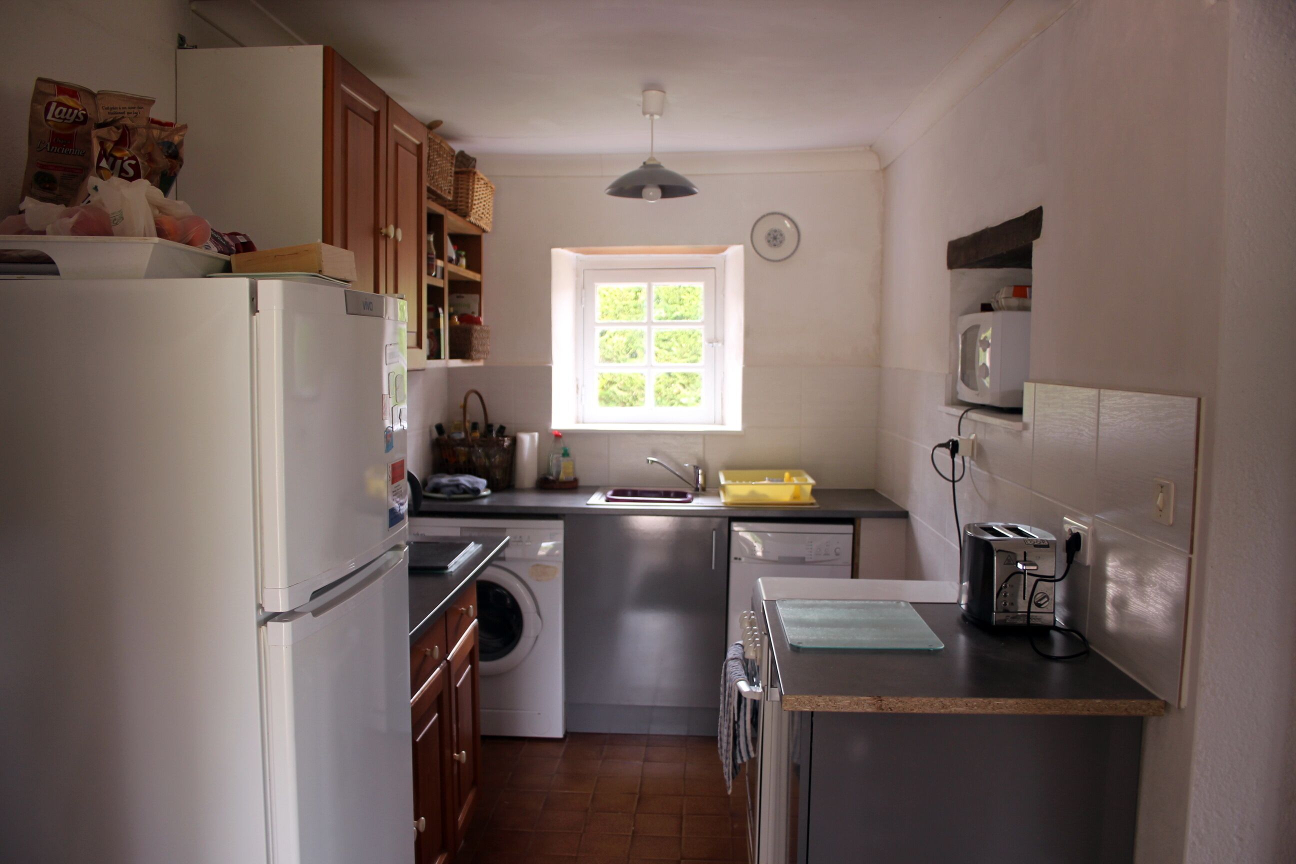 A compact kitchen with a refrigerator, washing machine, microwave, and a small island with a toaster.
