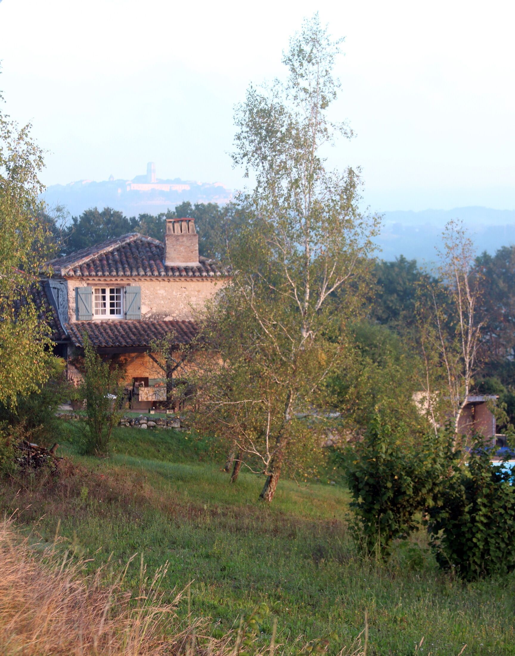 A rustic house with a tiled roof, surrounded by greenery and trees.