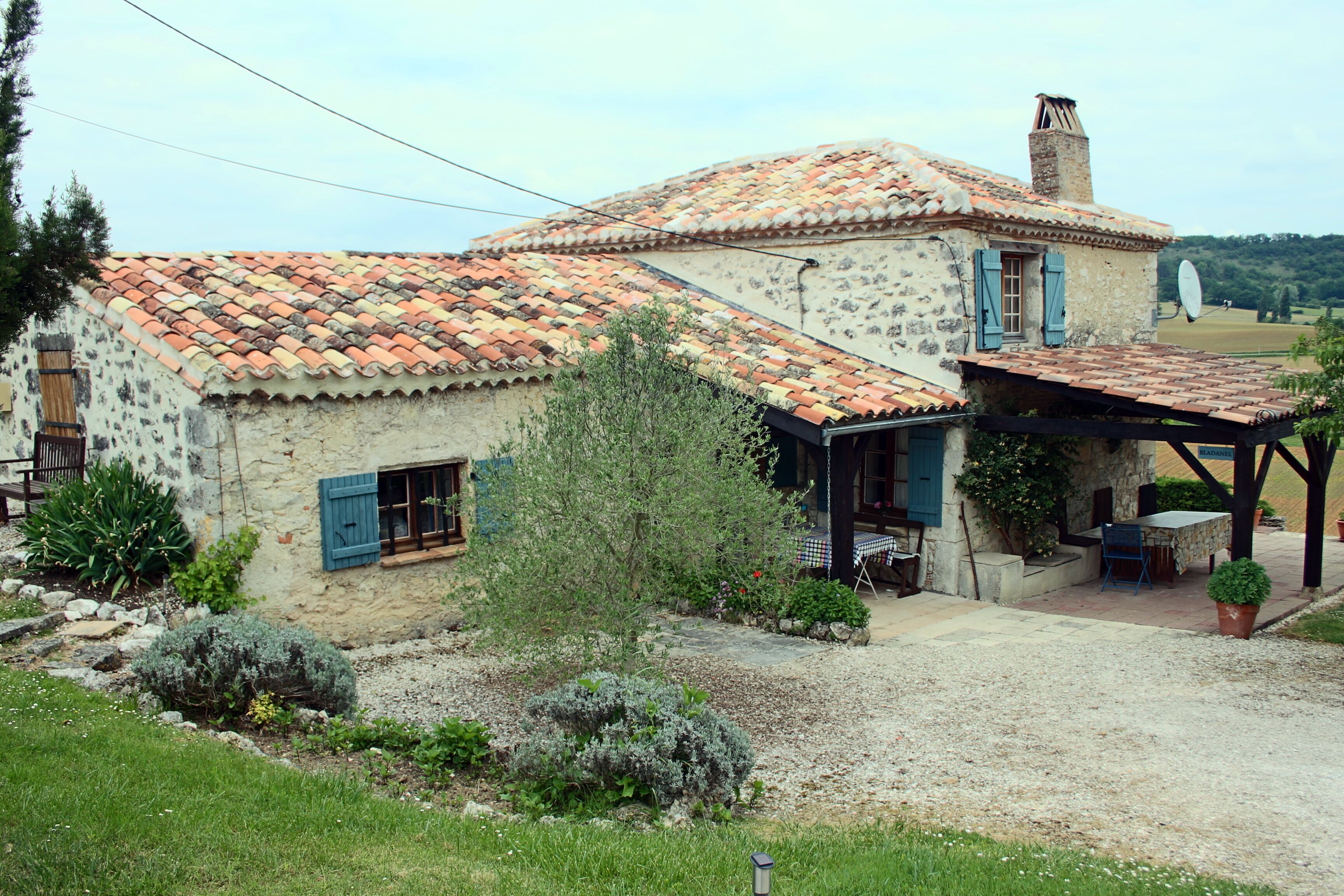 Una casa de piedra rústica con tejado de tejas, un porche cubierto y un jardín.