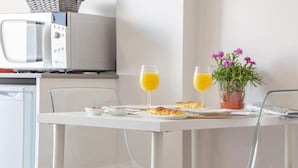 Ein Frühstückstisch mit zwei Orangensaftgläsern, einer Croissantplatte, einer kleinen Schale Beeren und einem Blumentopf mit violetten Blüten.