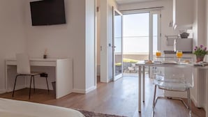 Ein modernes Hotelzimmer mit einem weißen Schreibtisch, einem Flachbildfernseher, einem Glastisch und Blick ins Freie.