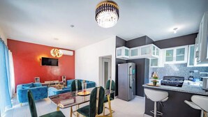 A modern living room with a dining area, a kitchen with a central island, and a TV mounted on the red wall. - Sosúa Modern Villa w/ Pool, BBQ & Near Nightlife (Sosúa)