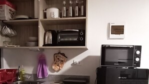 A kitchen with wooden cabinets, a microwave, a refrigerator, and a shelf with kitchen items. - Relaxing 1-Bedroom Condo Unit (by Lee Portum) (Marilao)