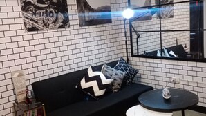 A modern living room with a black sofa, patterned cushions, a round table, and a large mirror reflecting the room. - Relaxing 1-Bedroom Condo Unit (by Lee Portum) (Marilao)