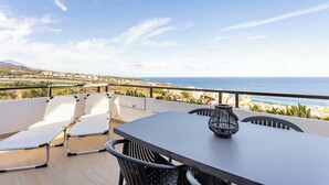 A terrace with a table and chairs, overlooking a coastal landscape.