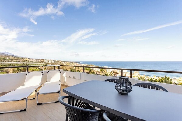 A terrace with a table and chairs, overlooking a coastal landscape.