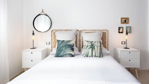 A bedroom with a large bed, two bedside tables, a round mirror, and wall-mounted pictures.