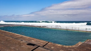 A swimming pool with a view of the ocean and waves crashing onto the shore.