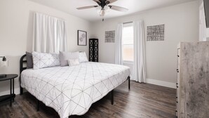 A bedroom with a bed, a ceiling fan, a nightstand, and a window with curtains.