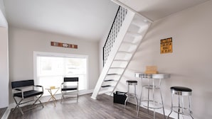 A modern living room with a wooden floor, a white staircase, a gaming room sign, and a caution sign.