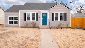 A single-story house with a blue door, numbered 2907, and a small front yard with a concrete path leading to the door.