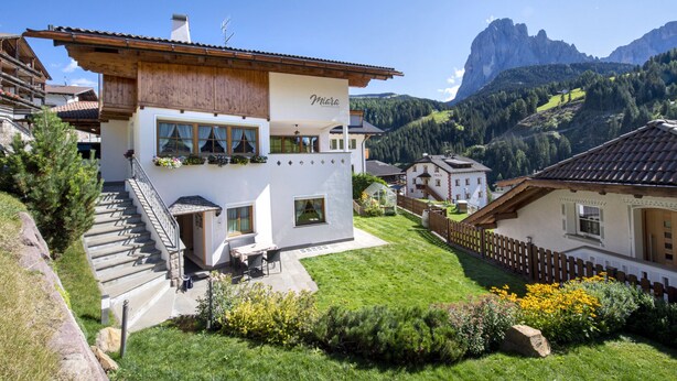 A two-story building with a white facade, a wooden balcony, and a view of a mountainous landscape.