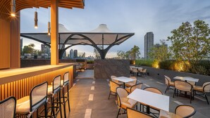 An outdoor seating area with tables and chairs, a bar, and a view of the city skyline. - Ramada Plaza by Wyndham Bangkok Sukhumvit 48 (Bangkok)