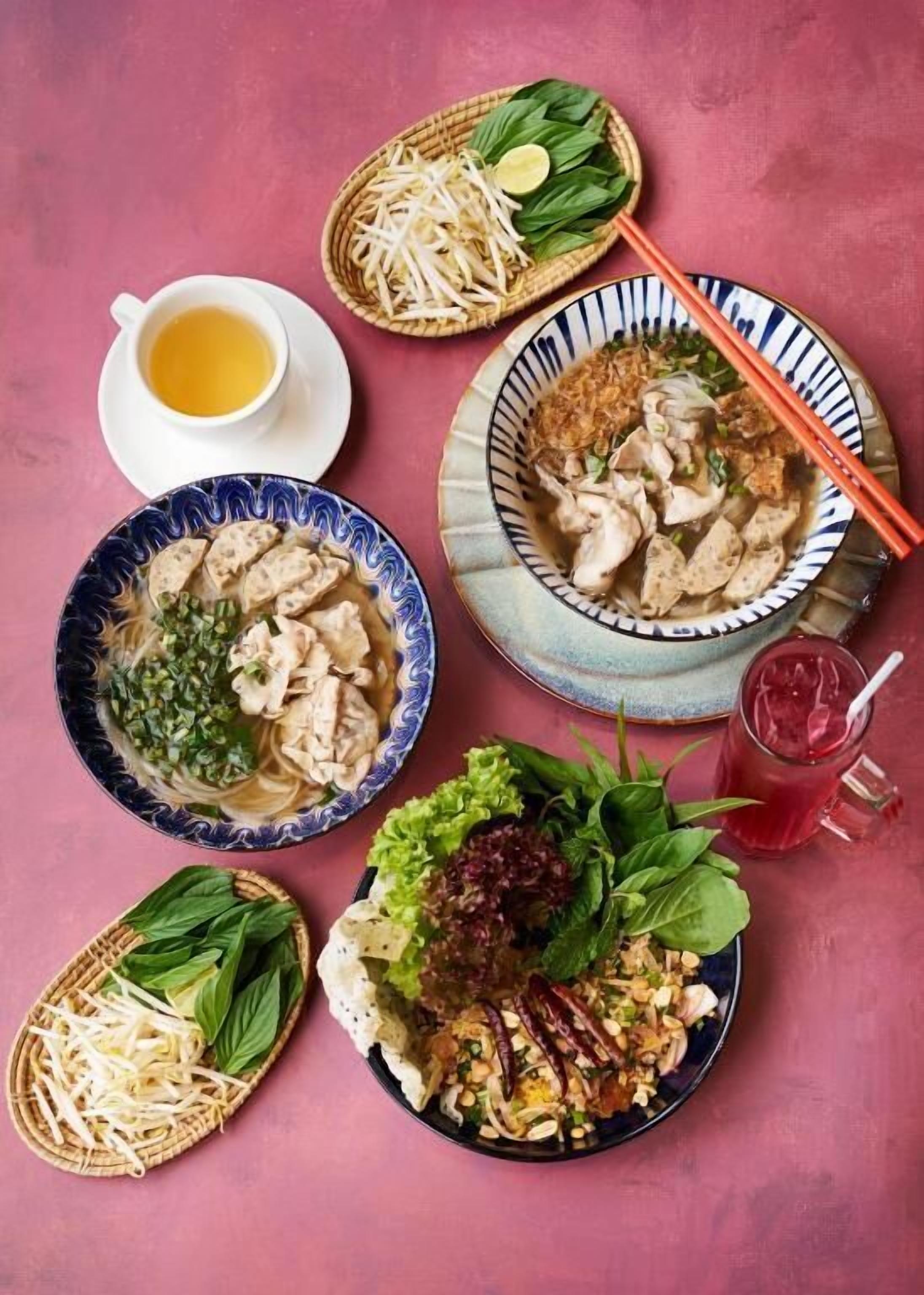 A table with various dishes including noodles, a bowl of soup, and a plate with vegetables and nuts.