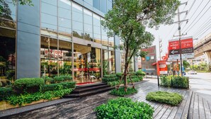 A modern building with a glass facade, a wooden walkway, and green landscaping. - Ramada Plaza by Wyndham Bangkok Sukhumvit 48 (Bangkok)
