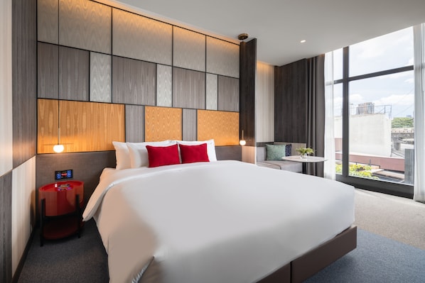 A modern hotel room with a large bed, a small table, and a view of the city through large windows. - Ramada Plaza by Wyndham Bangkok Sukhumvit 48 (Bangkok)
