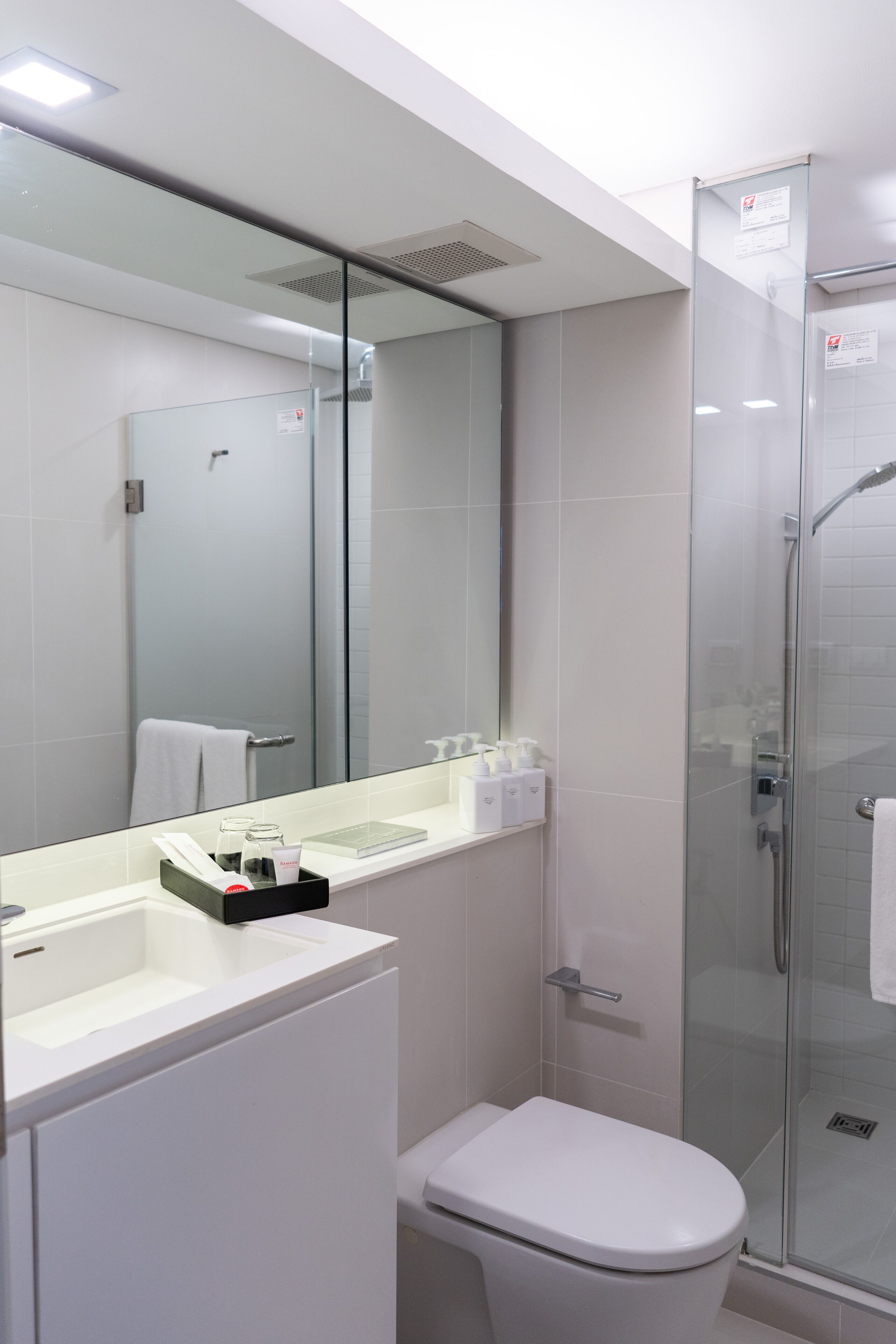 Un baño moderno con cabina de ducha de vidrio, inodoro blanco y tocador con espejo y encimera.