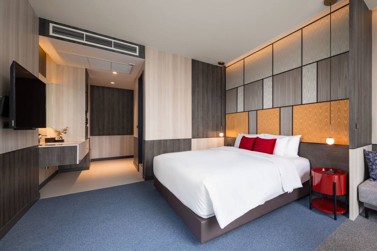 A modern hotel room with a large bed, a sofa, a TV, and a bathroom.