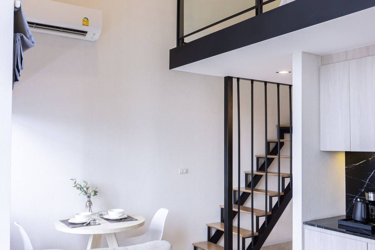 A modern apartment with a living area featuring a sofa, a dining table, and a kitchen with a black staircase.