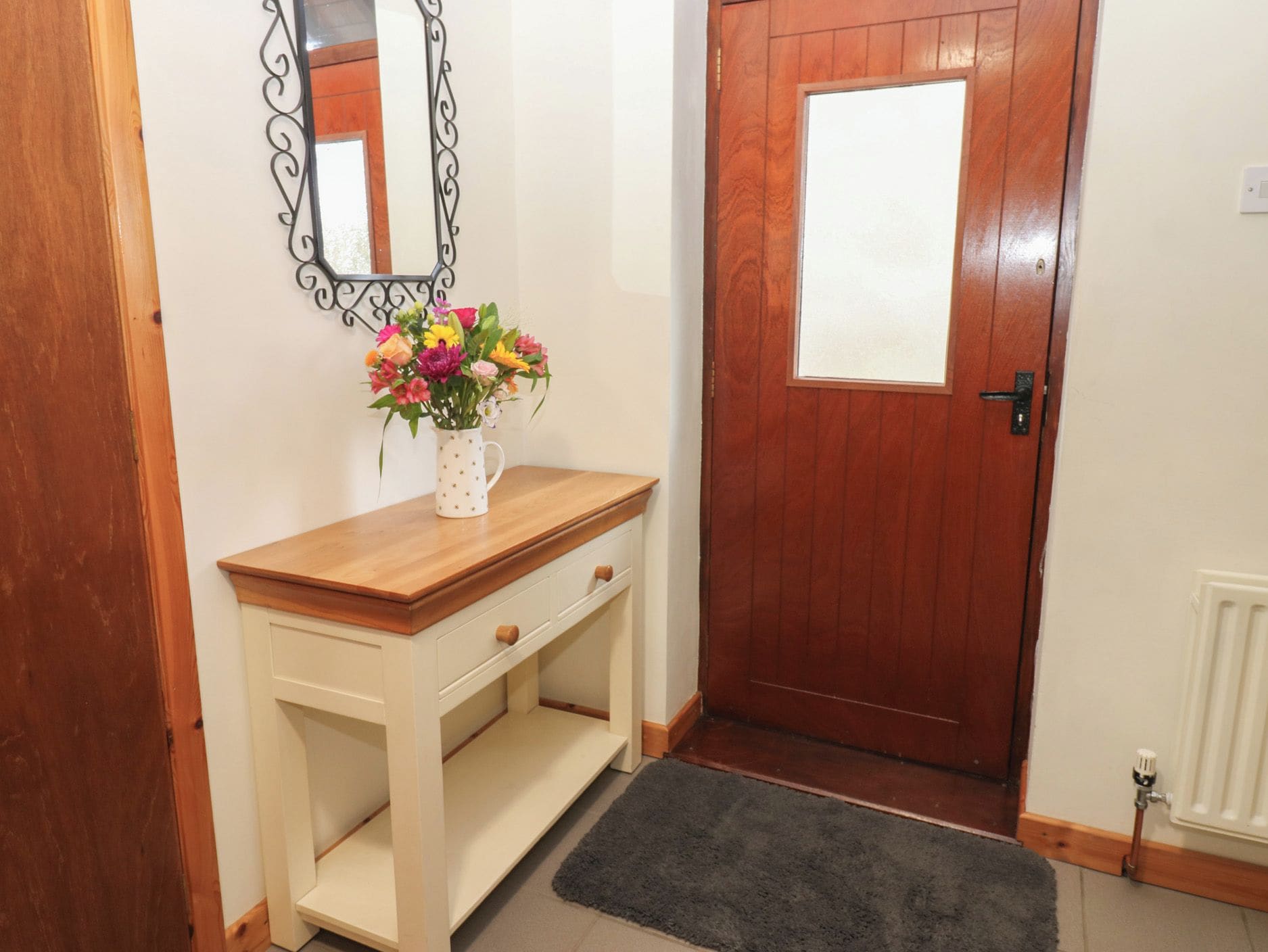 A wooden console table with a vase of flowers, a mirror, and a door with a window.