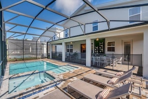 A covered outdoor swimming pool area with lounge chairs and a patio table, surrounded by a glass enclosure.