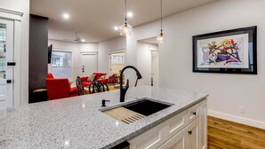 A modern kitchen with granite countertops, a sink, and pendant lighting. There is a dining area with a red sofa and a table in the background. - Excellent 3BR/2BA PRIME Location! (Louisville)