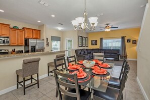 A modern kitchen with wooden cabinets, a stainless steel refrigerator, and a dining area with a glass table set for six.