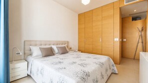 Een slaapkamer met een bed, nachtkastje, lamp, kast en een deur naar een andere kamer.