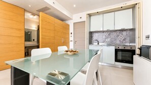 Uma cozinha moderna com mesa de jantar de vidro, cadeiras brancas e backsplash estampado.