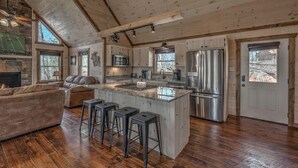 A spacious kitchen with a large island, wooden flooring, and a stone fireplace. - Wolfs Den II - Shuffleboard | Foosball | Fire Pit | Outdoor Wood Burning Fireplace (Blue Ridge)