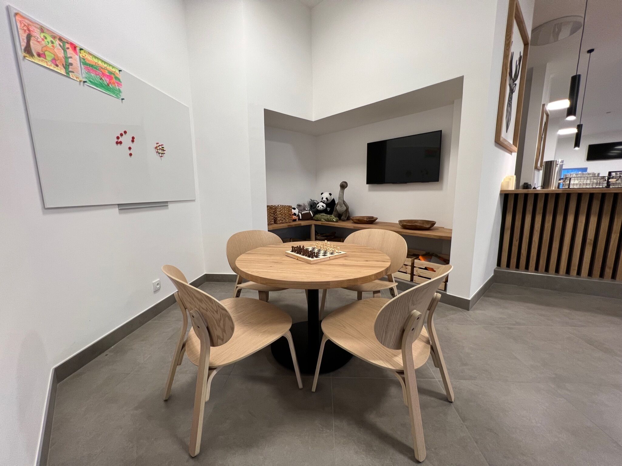 Una sala de reuniones moderna con una mesa redonda de madera, cuatro sillas, una pizarra, un televisor y una estantería con adornos.