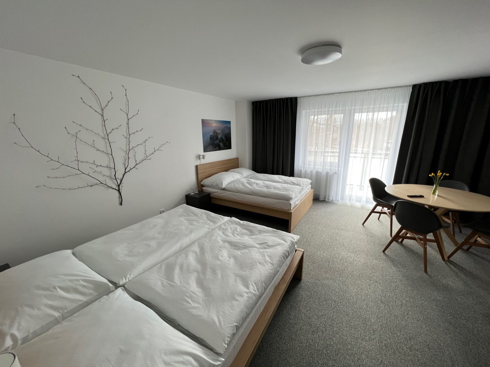 A hotel room with two single beds, a small table with chairs, a wall-mounted branch decoration, and a painting.