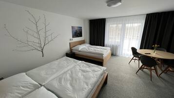 A hotel room with two single beds, a small table with chairs, a wall-mounted branch decoration, and a painting.