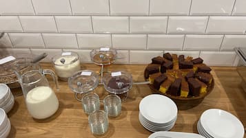 Mesa de buffet com diversos alimentos, incluindo um bolo, tigelas de sopa e um jarro de leite.