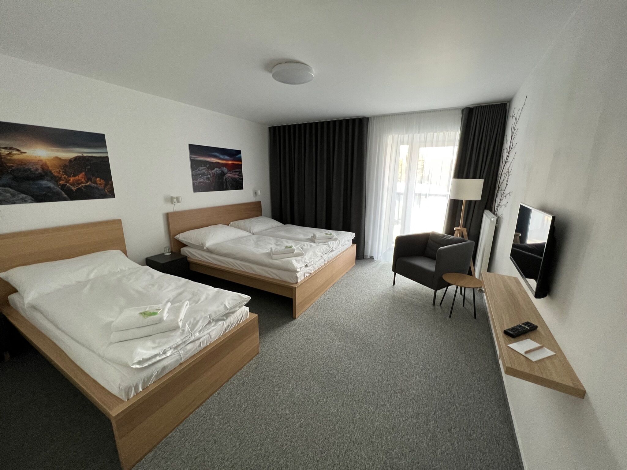 A hotel room with two single beds, a desk with a chair, a TV, and artwork on the walls.