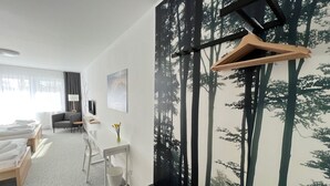 Una habitación de hotel moderna con una cama, un escritorio, una silla, un televisor y un mural temático de bosque.