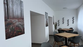A modern dining area with wooden tables and black chairs, white walls, and framed artwork.