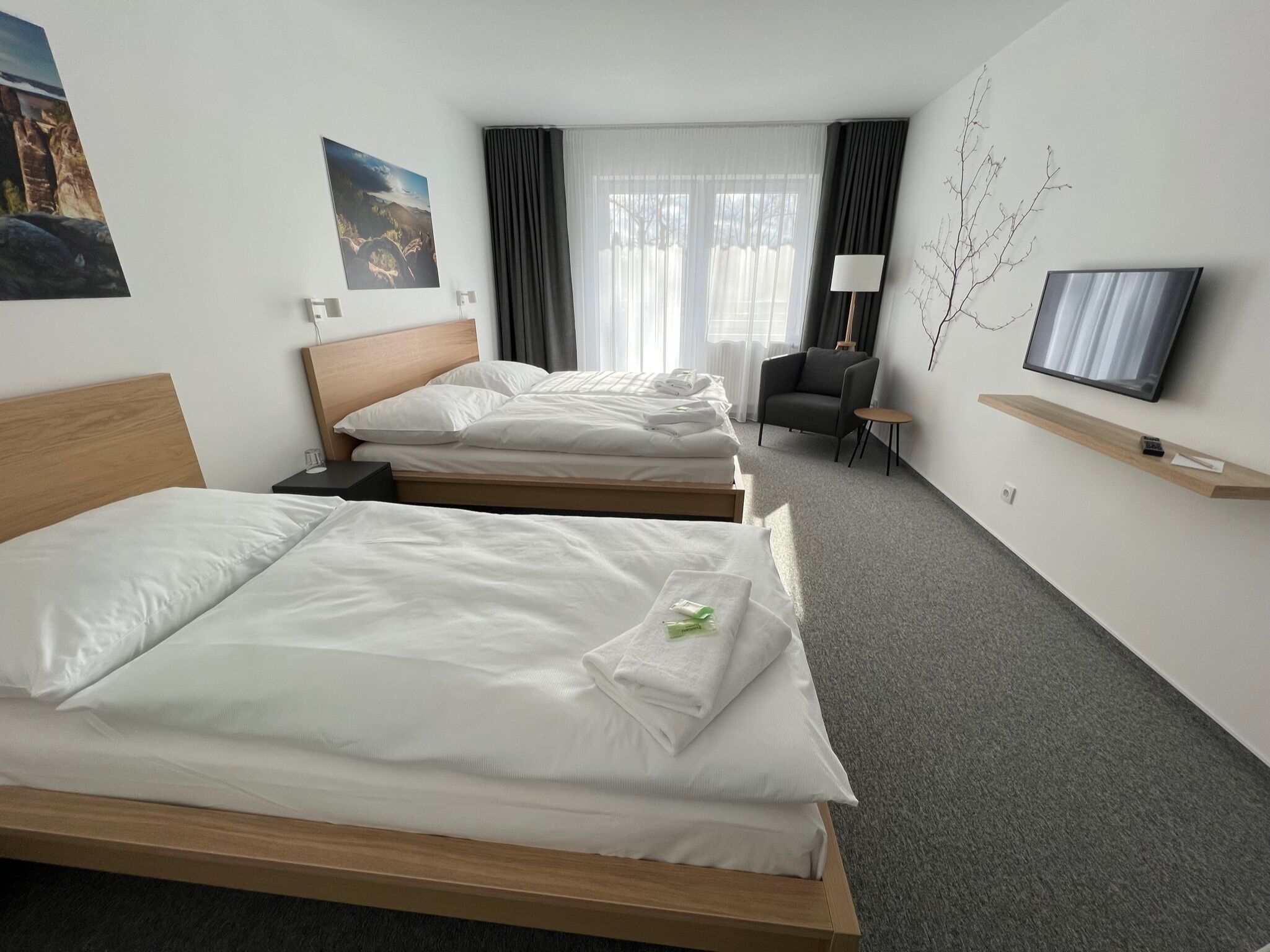 Ein Hotelzimmer mit zwei Betten, einem Fernseher, einem Sessel und einem kleinen Tisch.