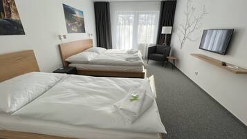Ein Hotelzimmer mit zwei Betten, einem Fernseher, einem Sessel und einem kleinen Tisch.