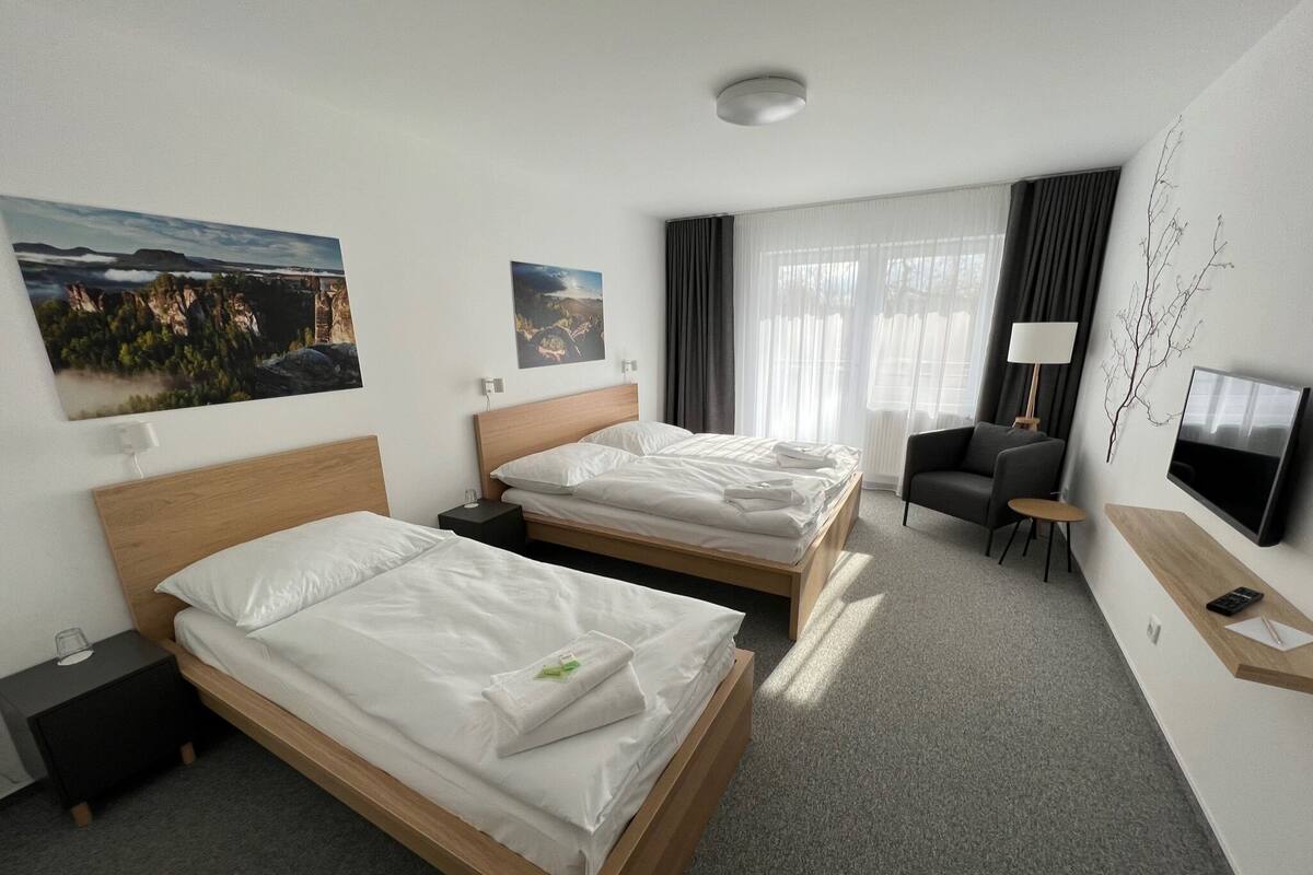 Ein Hotelzimmer mit zwei Betten, einem Fernseher, einem Schreibtisch und einem Sessel.