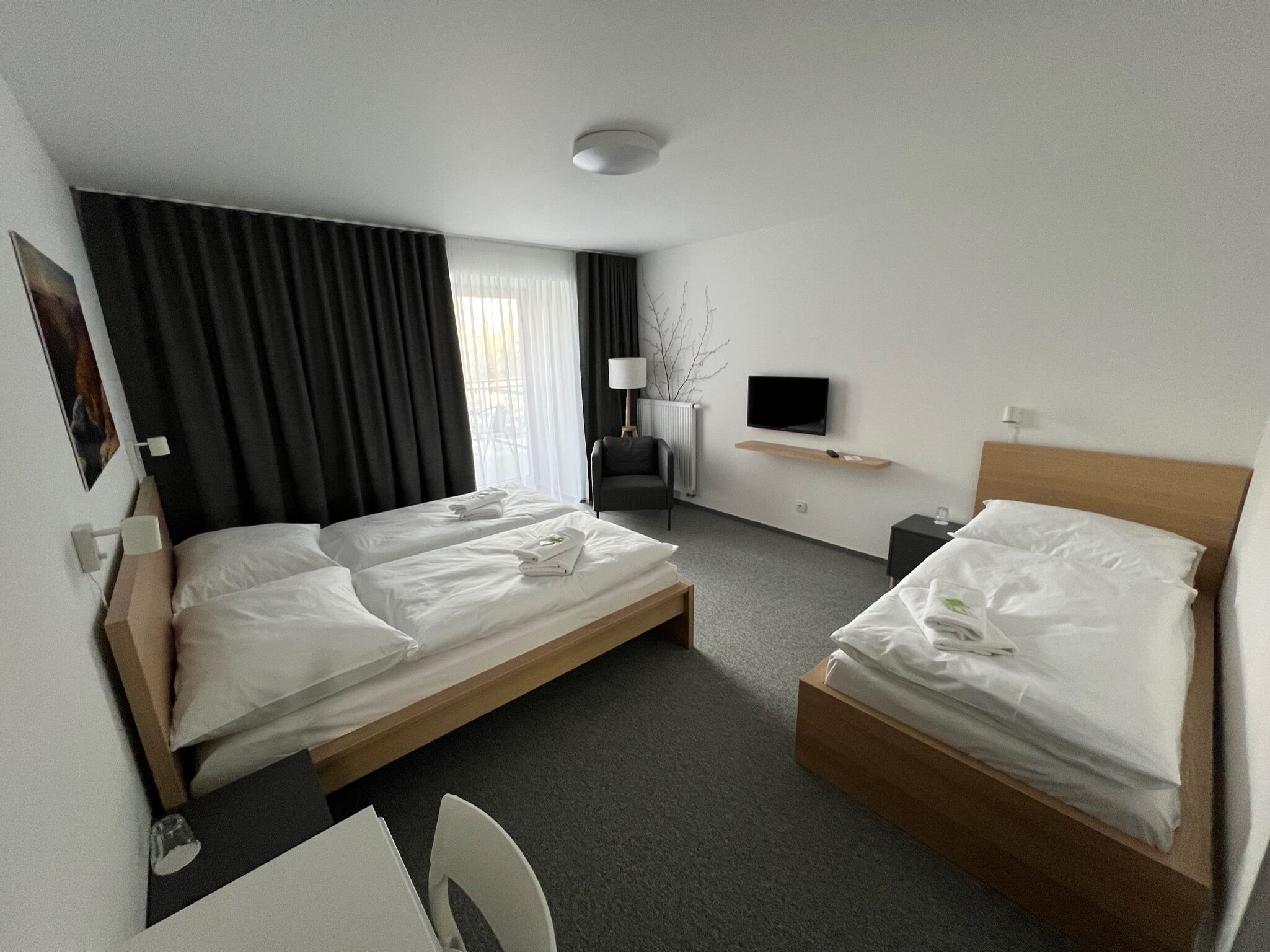 Quarto de hotel com duas camas de solteiro, uma escrivaninha, uma cadeira, uma televisão e uma janela com cortinas.