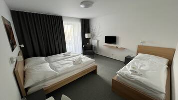 Quarto de hotel com duas camas de solteiro, uma escrivaninha, uma cadeira, uma televisão e uma janela com cortinas.