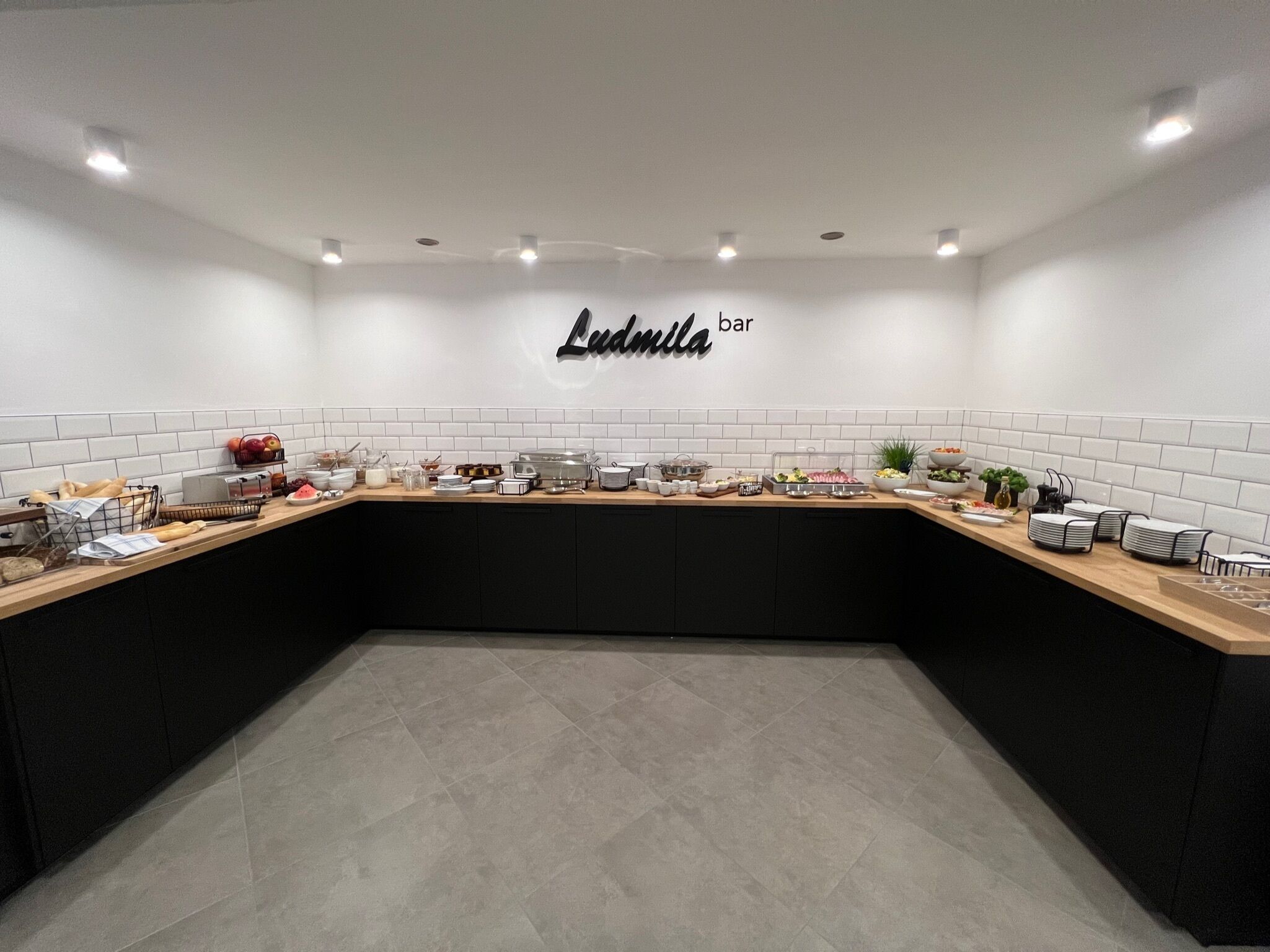 Una cocina moderna con encimera curva, salpicadero blanco de azulejos y un letrero que dice "Ludmila bar".