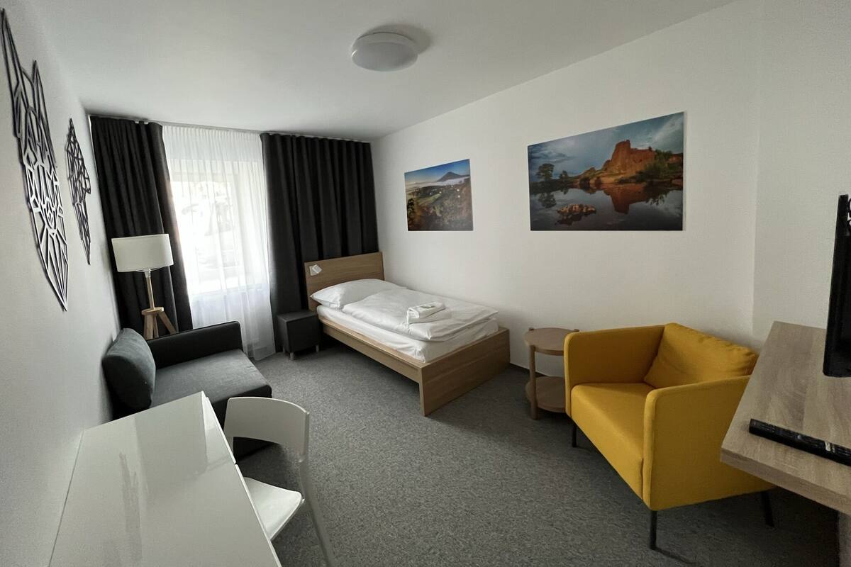 Ein Hotelzimmer mit Bett, Schreibtisch, Stuhl, Sofa, Fernseher und zwei Bildern an der Wand.