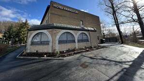 Un hotel llamado "HOTEL VARNSDORF" con fachada de ladrillo, ventanas arqueadas y una zona de estacionamiento.