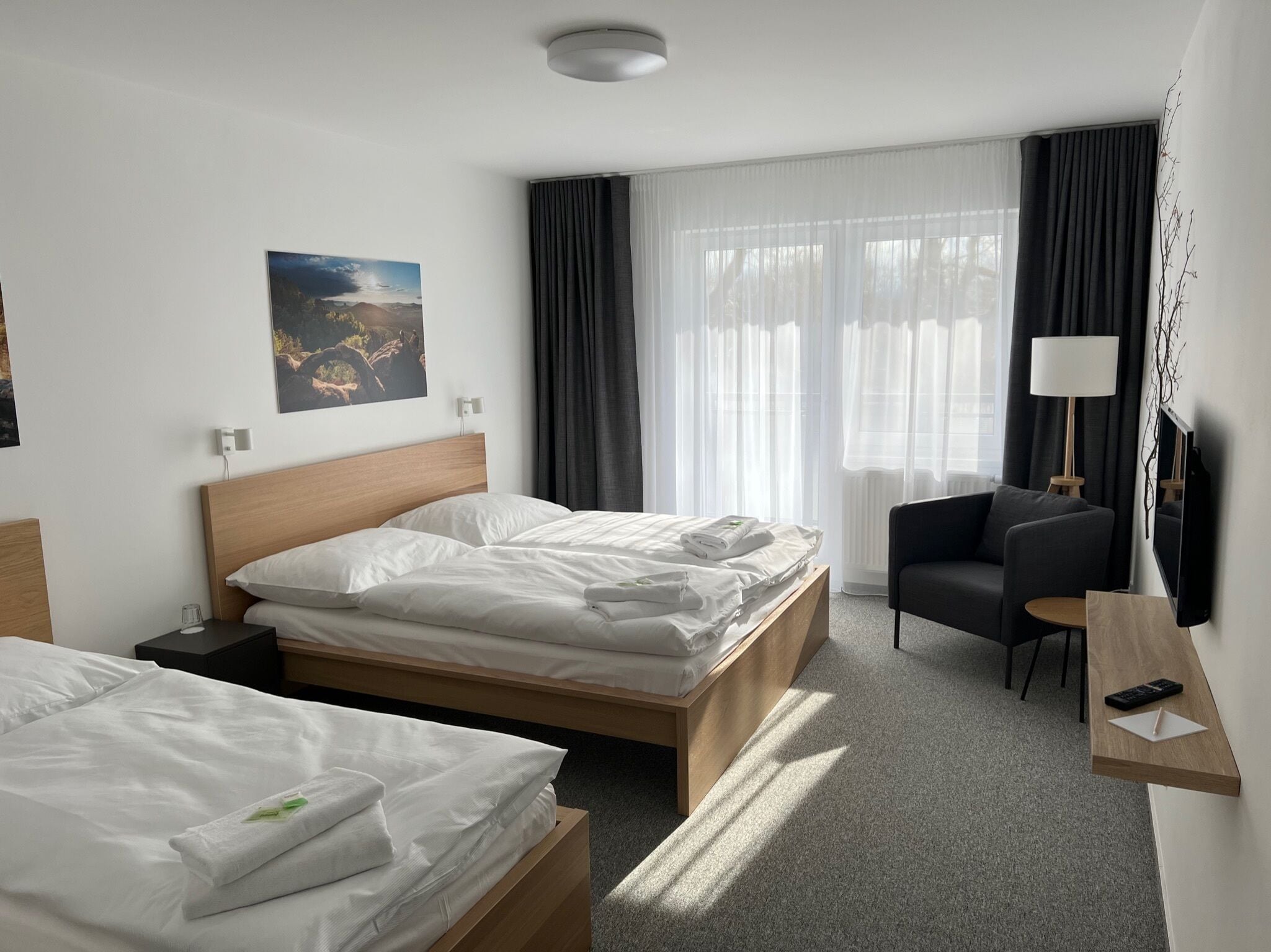 Habitación de hotel con dos camas, un escritorio con silla, un televisor y un cuadro en la pared.